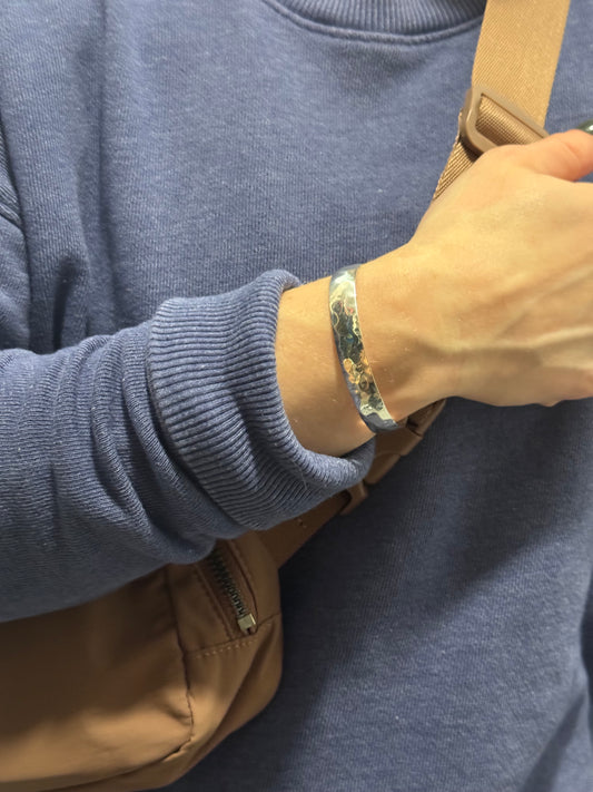 Person wearing a floral-patterned bracelet on a blue sweater with a brown bag in the background