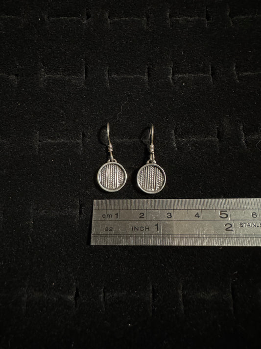 Two silver badminton racket earrings on a dark textured surface with a ruler for scale.