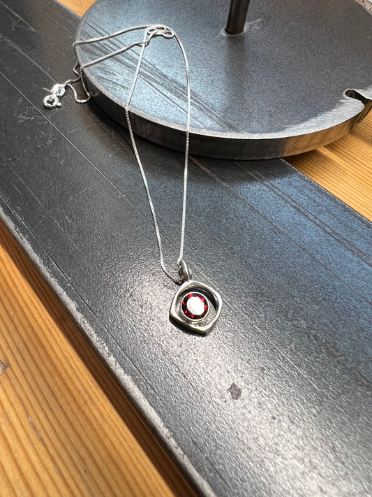 Square-Ring Pendant with Faceted Garnet – close-up of sterling silver square ring pendant showing faceted red garnet stone bezel detail, black background
