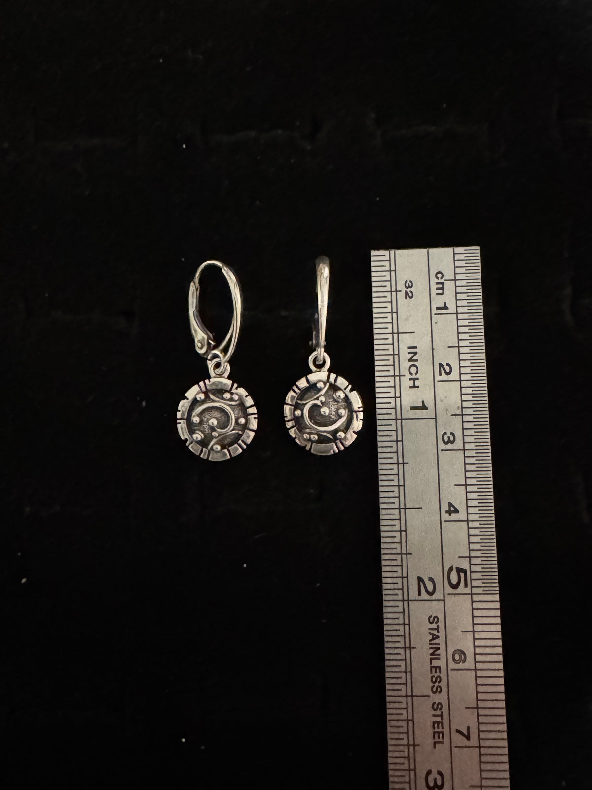 Silver earrings with a ruler for scale on a black background