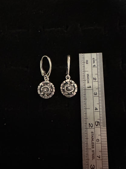 Silver earrings with a ruler for scale on a black background
