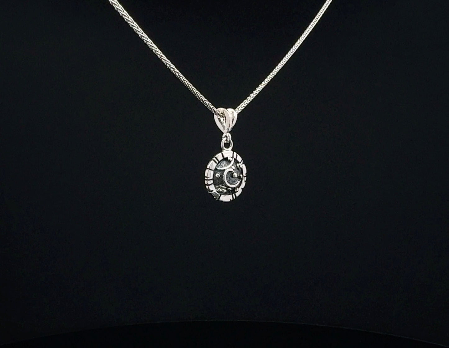 A silver chain necklace with a circular pendant featuring a crescent moon and star design, displayed against a solid black background.