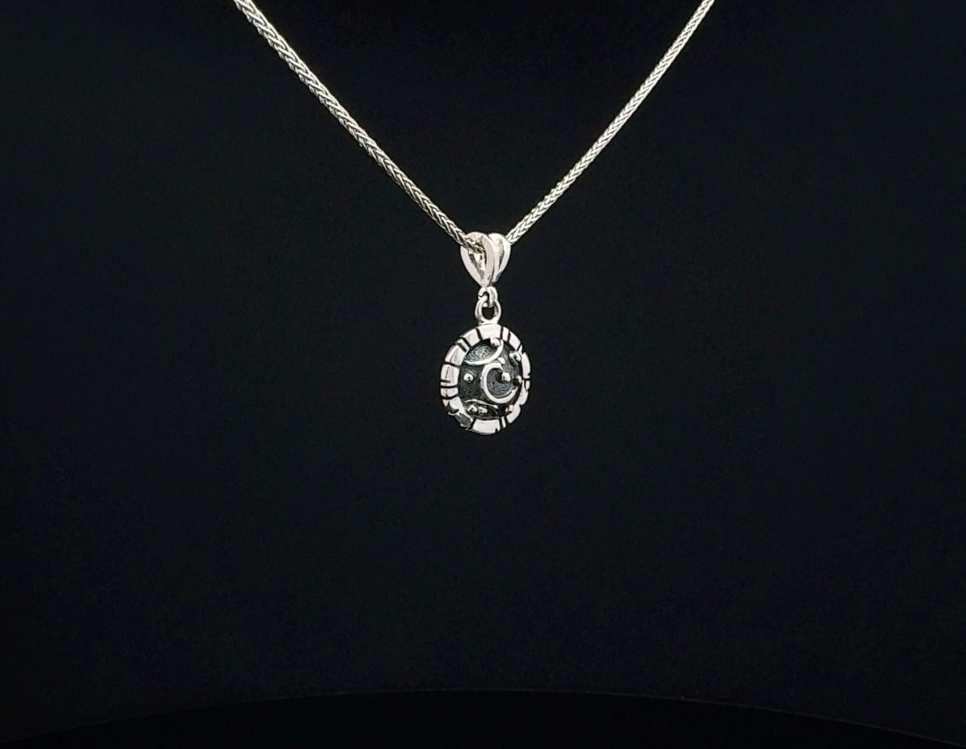 A silver chain necklace with a circular pendant featuring a crescent moon and star design, displayed against a solid black background.