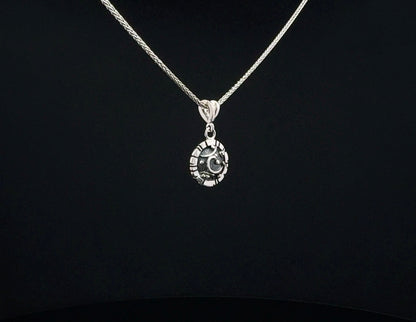 A silver chain necklace with a circular pendant featuring a crescent moon and star design, displayed against a solid black background.