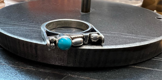 A sterling silver bar ring with turquoise and rose gold accents displayed on a textured surface.