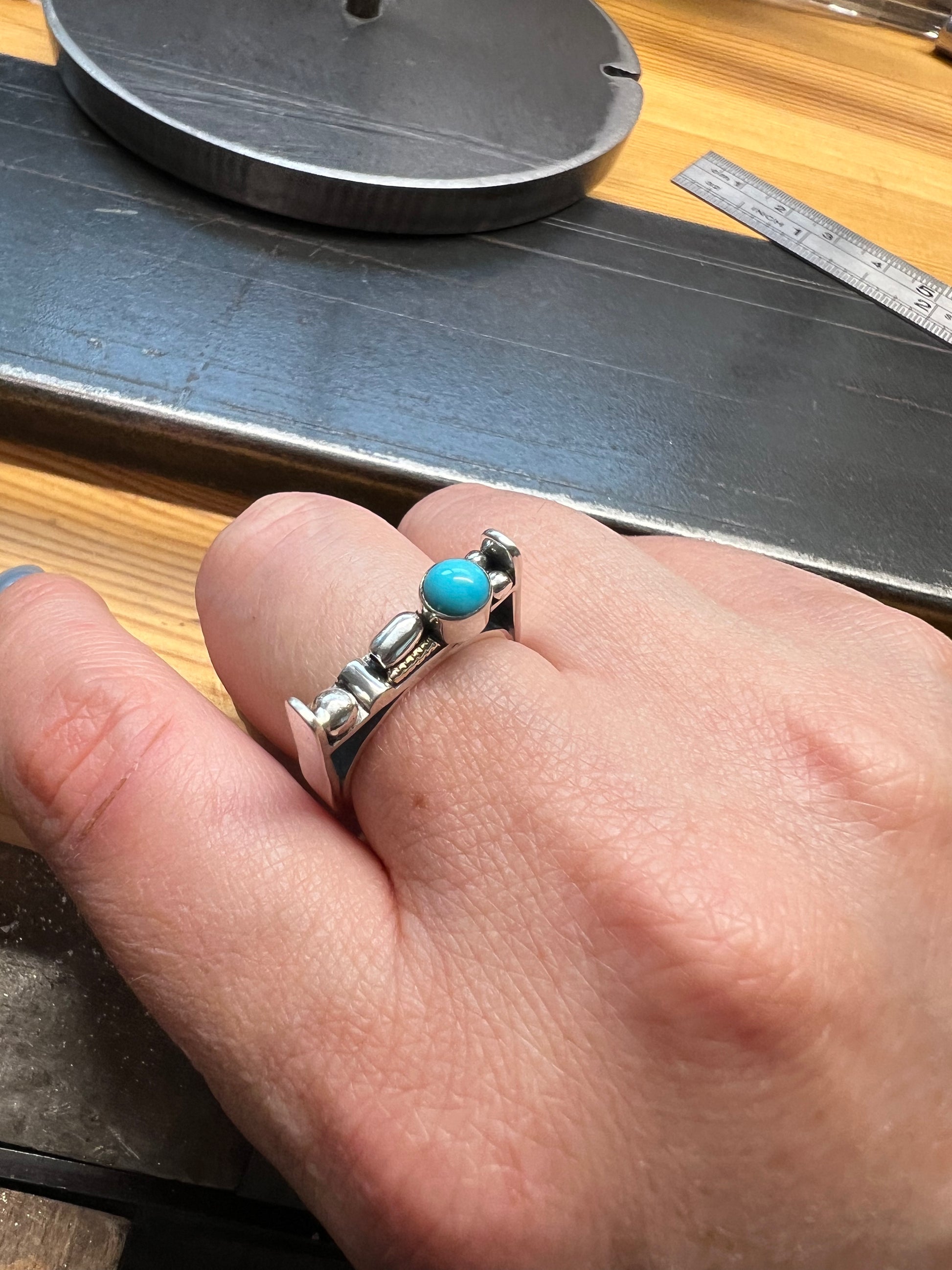 Sterling Silver Bar Ring with Turquoise and Rose Gold Accents – lifestyle shot of handcrafted sterling silver bar ring with turquoise and rose gold accents worn on finger, black background