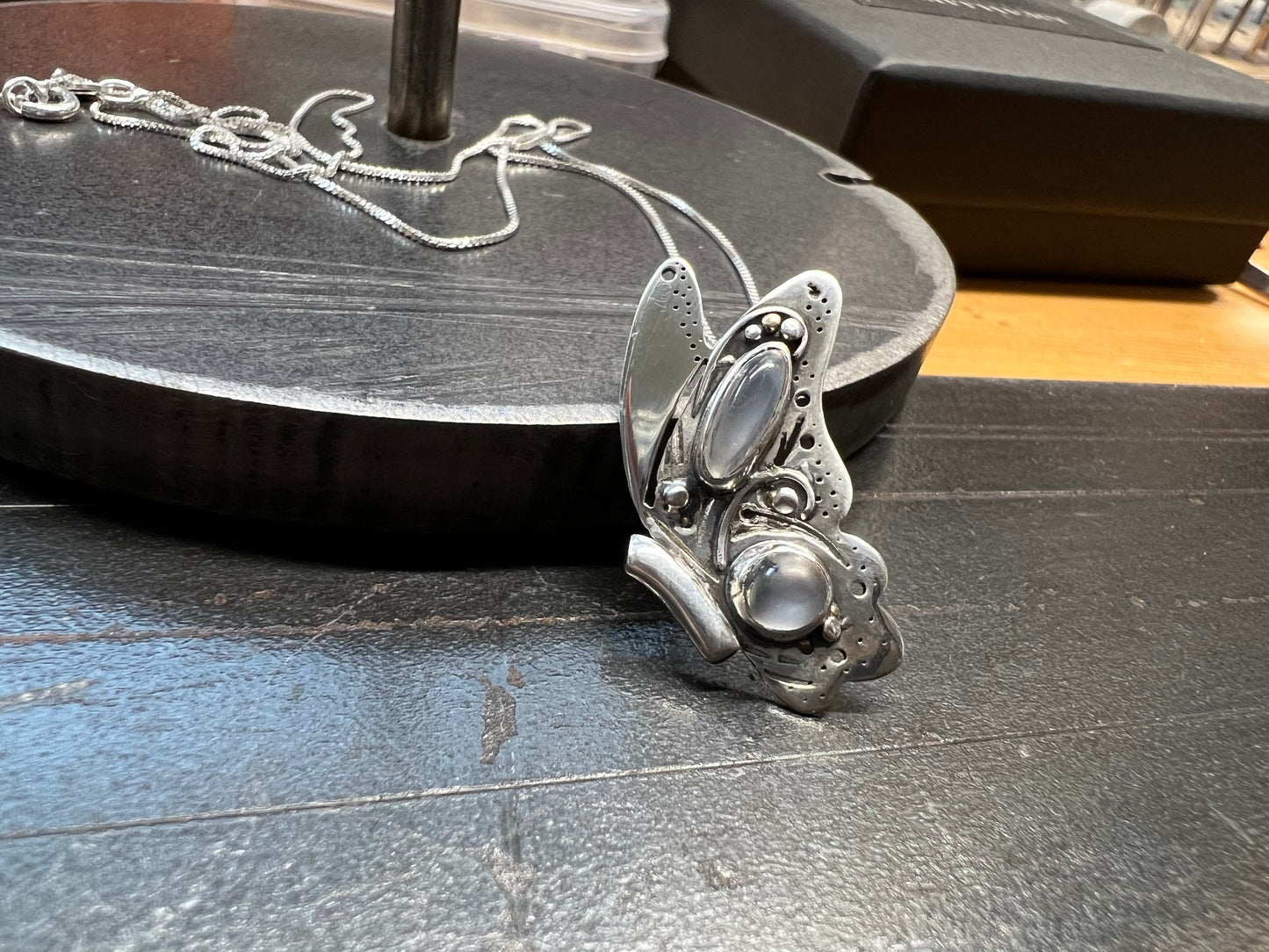 A sterling silver butterfly pendant with intricate design and grey moonstones, displayed on a dark surface.