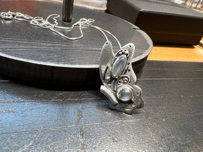 A sterling silver butterfly pendant with intricate design and grey moonstones, displayed on a dark surface.