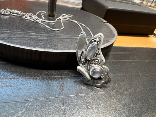 A sterling silver butterfly pendant with intricate design and grey moonstones, displayed on a dark surface.