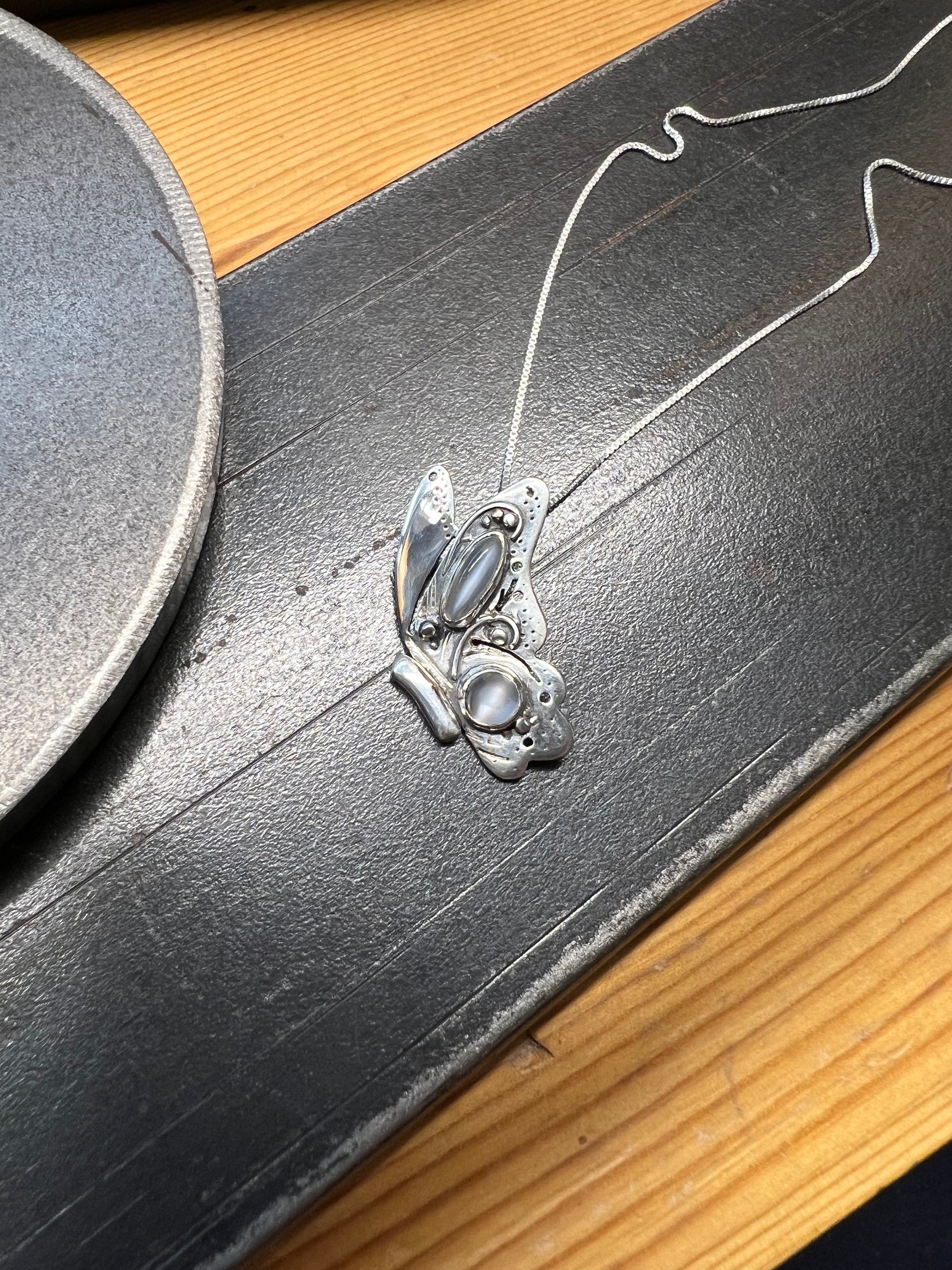 Sterling Silver Butterfly Pendant with Grey Moonstones – lifestyle shot of handcrafted sterling silver butterfly pendant with grey moonstone accents worn on neck, black background