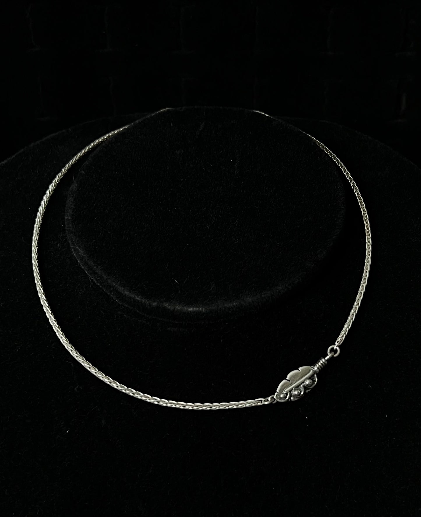A sterling silver necklace with an embedded feather-shaped pendant, displayed against a black background.