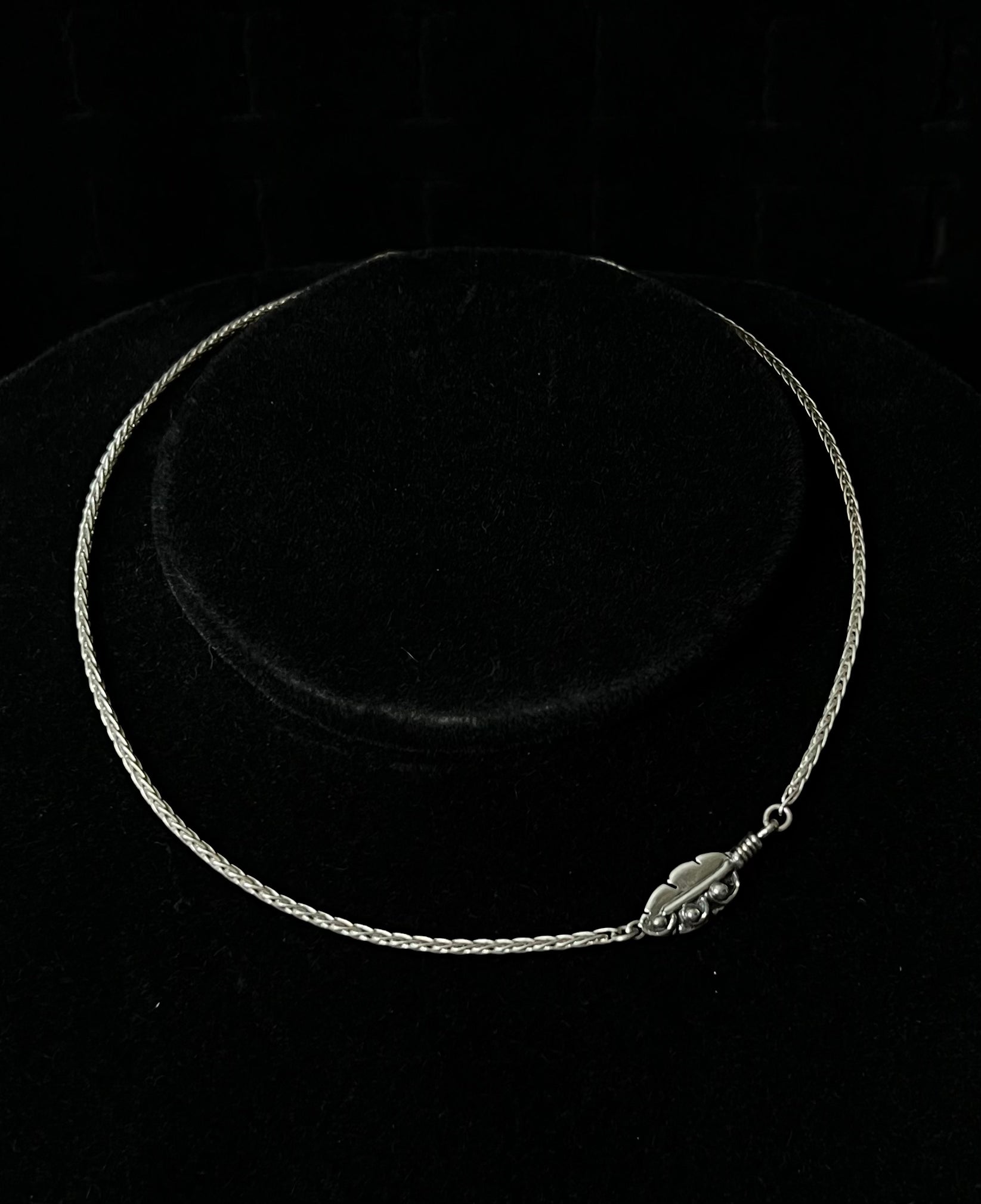 A sterling silver necklace with an embedded feather-shaped pendant, displayed against a black background.