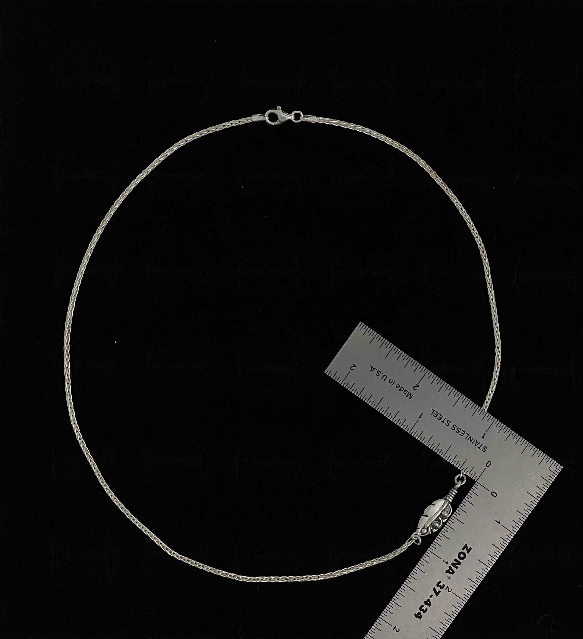 Embedded Feather Necklace – side view of sterling silver bezel-set resin pendant with natural feather detail on box chain, black background