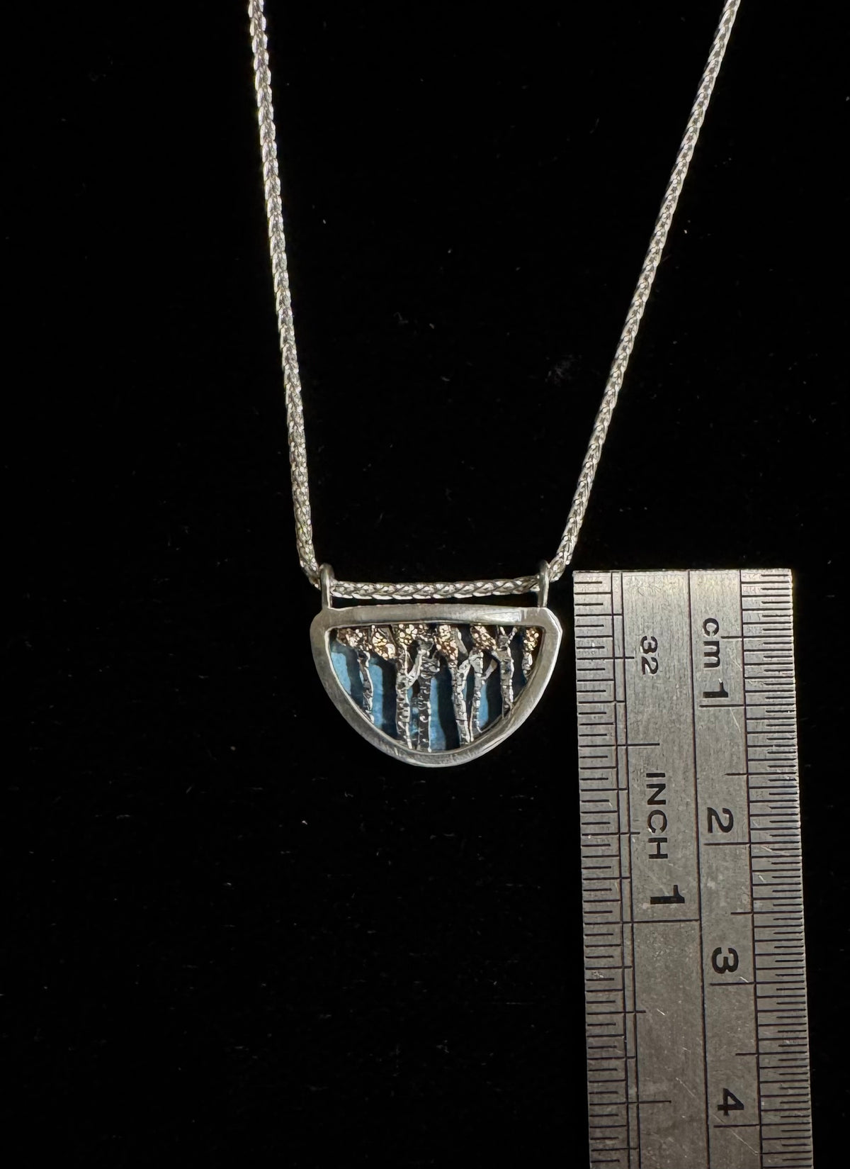 Silver necklace with a pendant next to a ruler on a black background