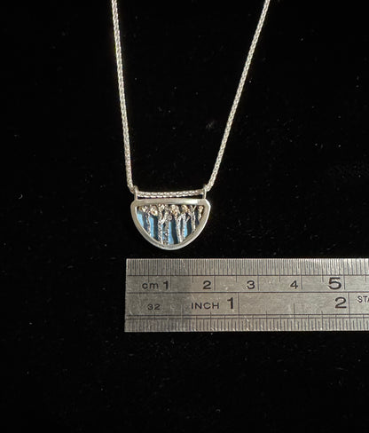 Silver necklace with a half-circle pendant on a black background, measured against a ruler.
