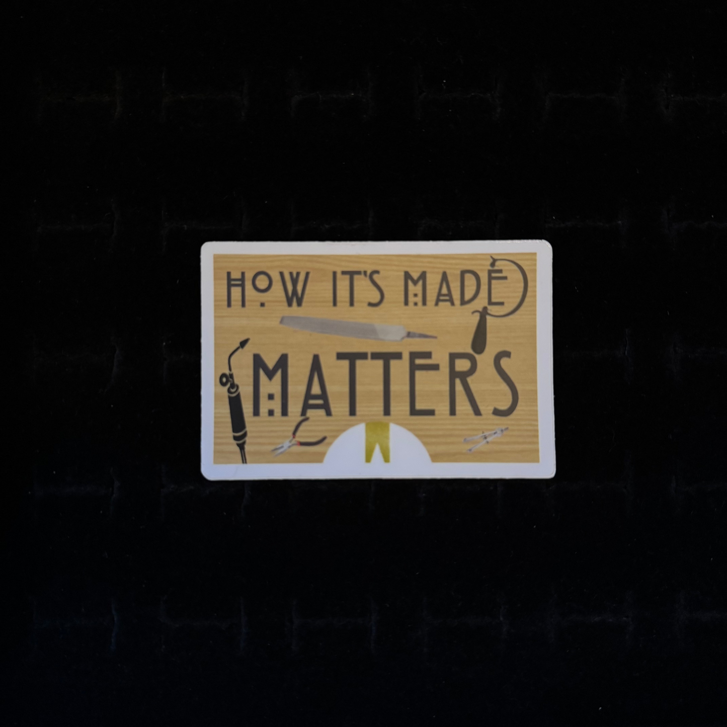 A rectangular sticker with the text 'HOW ITS MADE MATTERS' displayed on it, along with illustrations of crafting tools like a saw, torch, and pliers.
