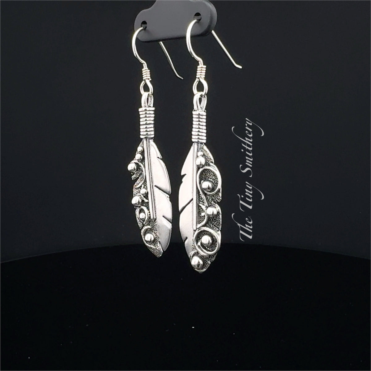 Silver feather-shaped earrings on a black background with 'The Wire Smithy' branding.