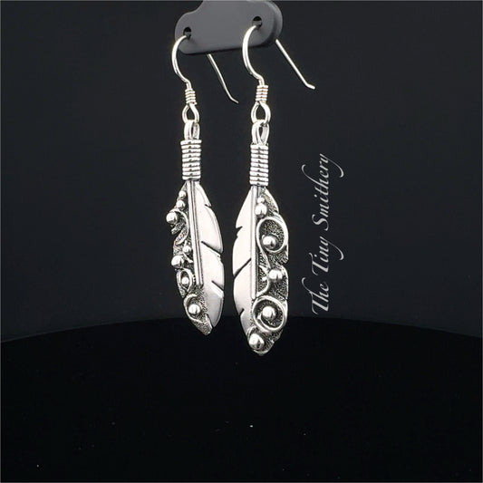 Silver feather-shaped earrings on a black background with 'The Wire Smithy' branding.