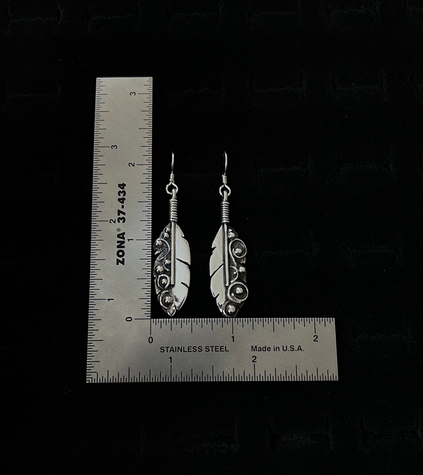 Long Feather Earrings – lifestyle shot of handcrafted sterling silver long oxidized feather drop earrings worn on ear, black background