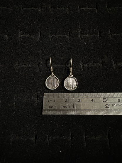 Two silver badminton racket earrings on a dark textured surface with a ruler for scale.