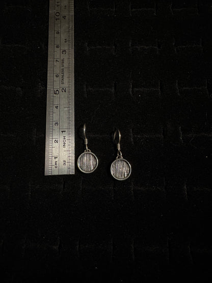 Pair of round earrings on a dark textured surface with a ruler for scale.