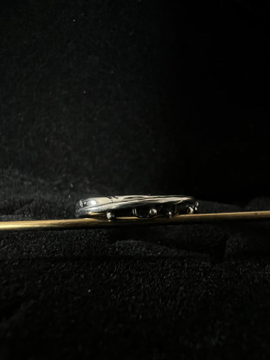 A close-up image of a silver ring with a feather design on a textured dark background.