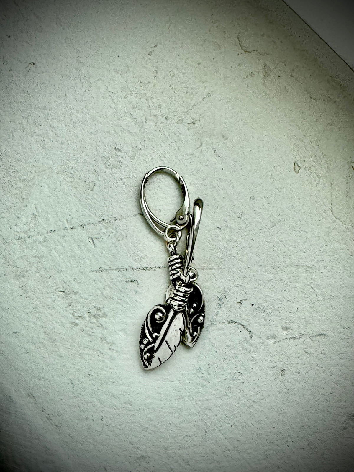 Silver leaf-shaped earring on a textured light gray background