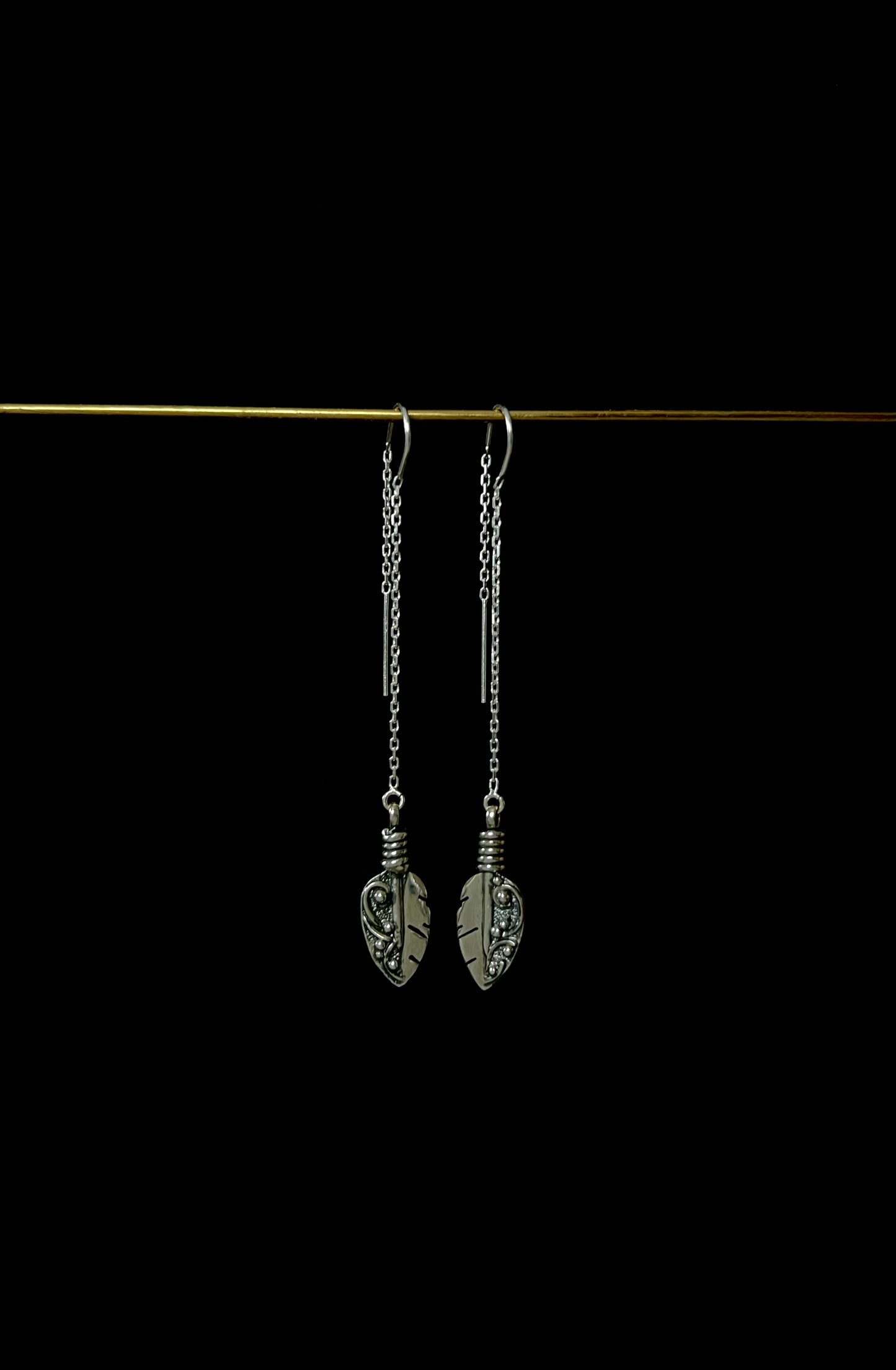 A pair of sterling silver threader earrings with feather-like designs, displayed against a dark background.
