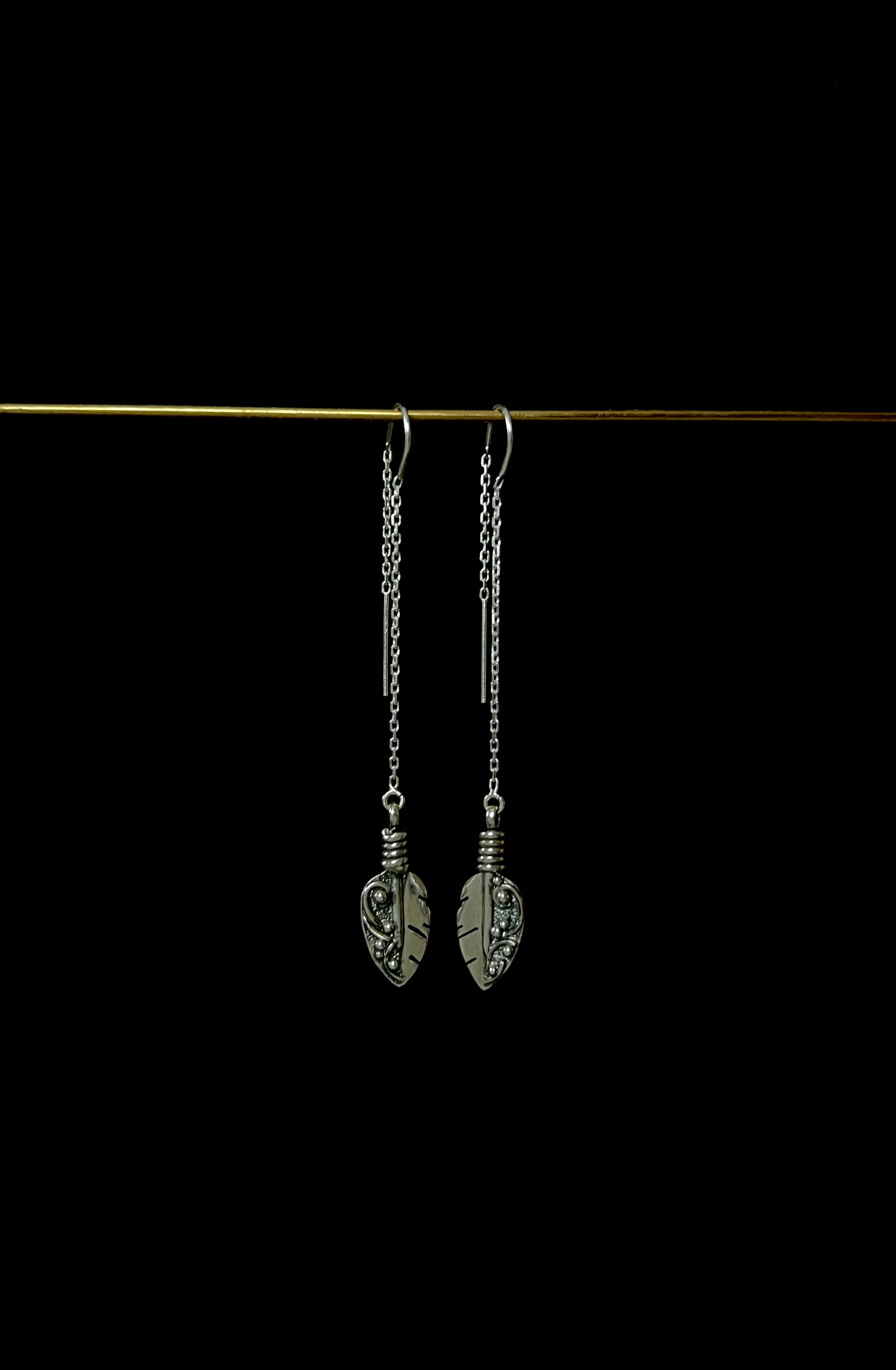 A pair of sterling silver threader earrings with feather-like designs, displayed against a dark background.