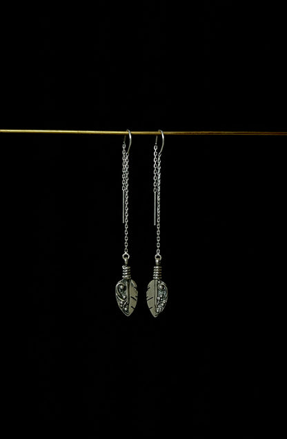 A pair of sterling silver threader earrings with feather-like designs, displayed against a dark background.