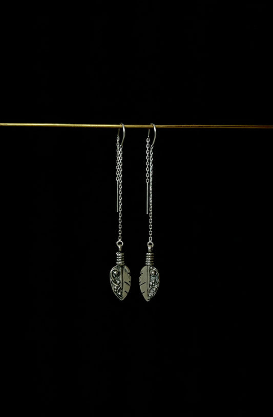 A pair of sterling silver threader earrings with feather-like designs, displayed against a dark background.