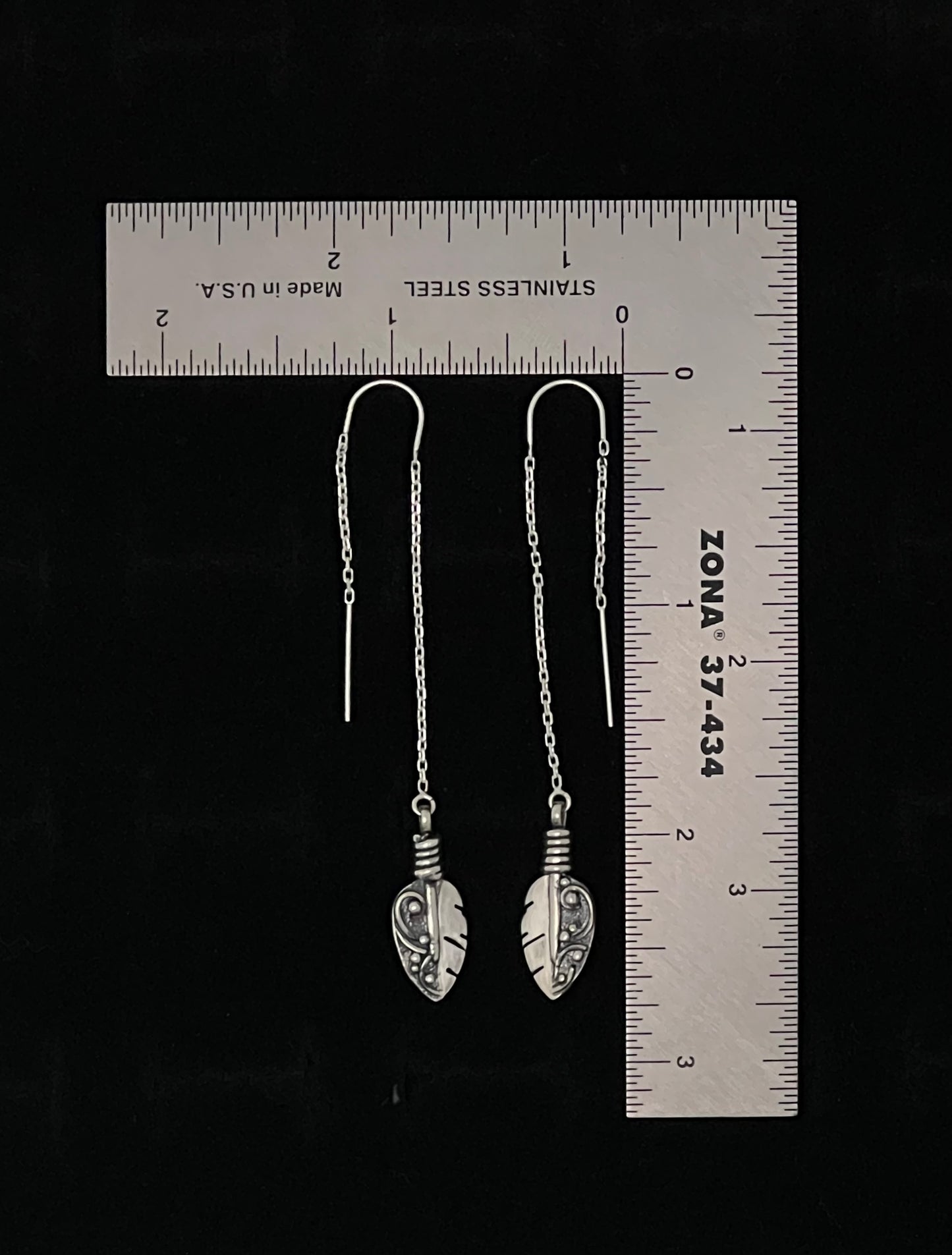 Petite Feather Threaders – lifestyle shot of handcrafted sterling silver petite feather threader earrings worn on ear, black background