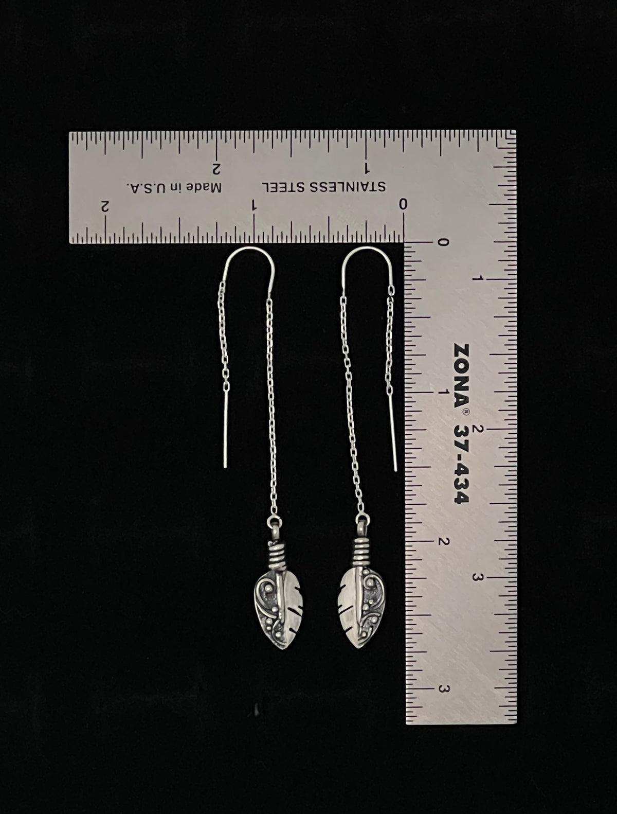 Petite Feather Threaders – lifestyle shot of handcrafted sterling silver petite feather threader earrings worn on ear, black background