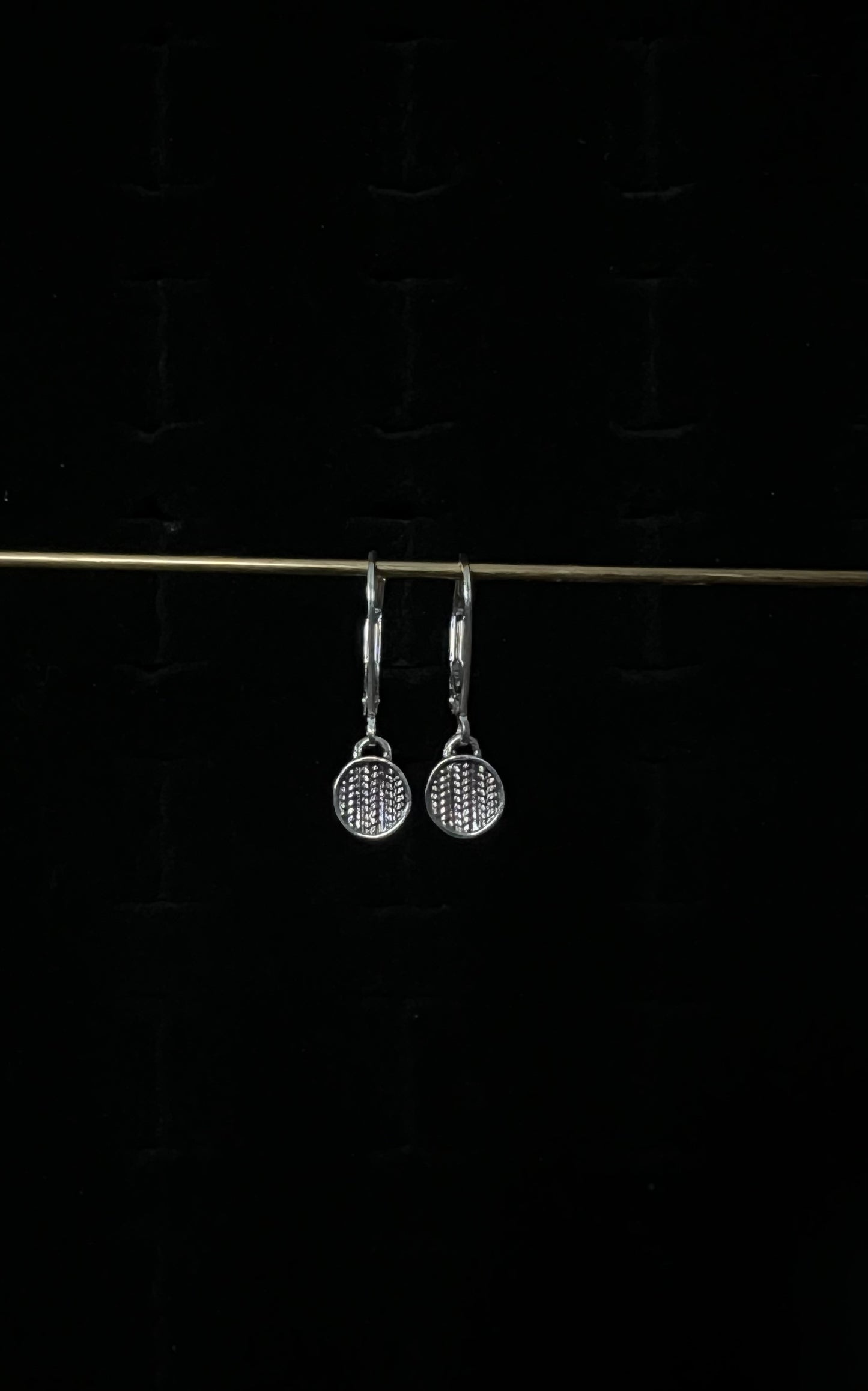 A pair of silver sweater drop lever back earrings displayed against a dark background.