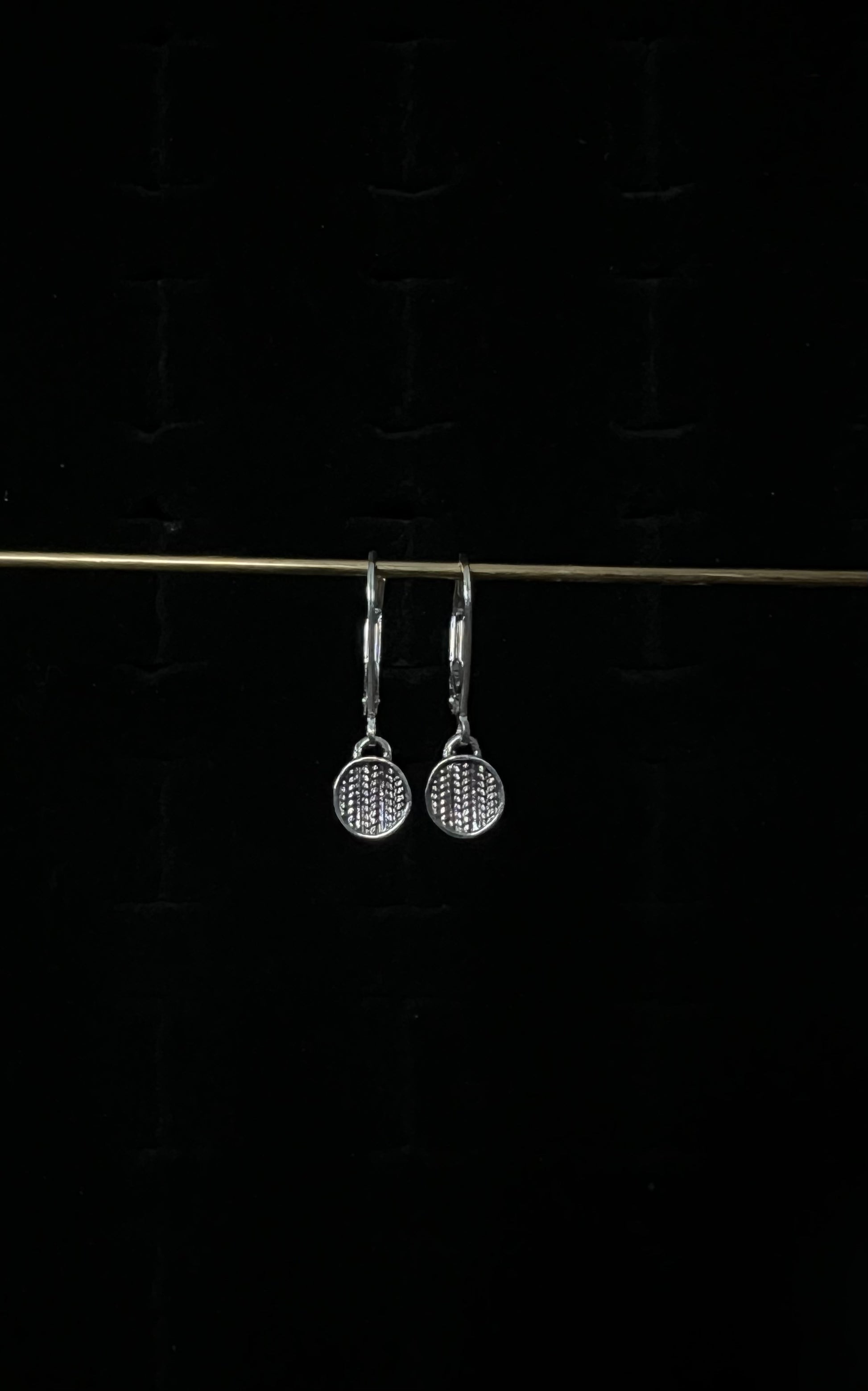 A pair of silver sweater drop lever back earrings displayed against a dark background.