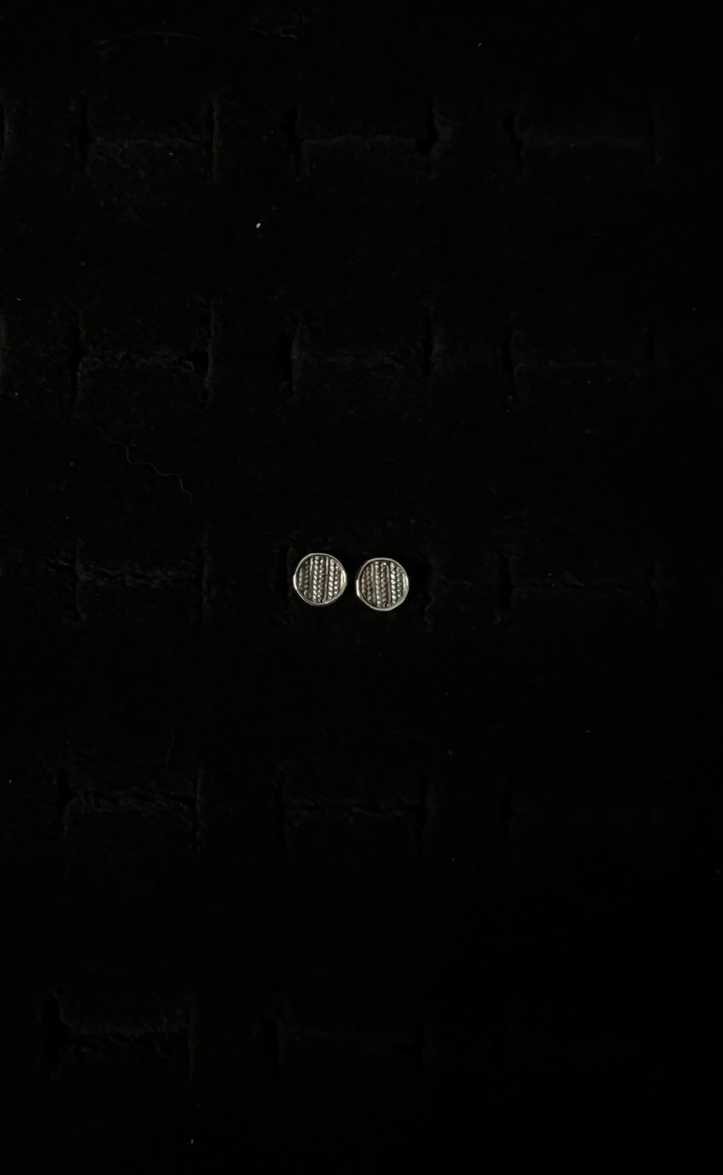 A close-up image of a pair of silver sweater post earrings on a textured black background.