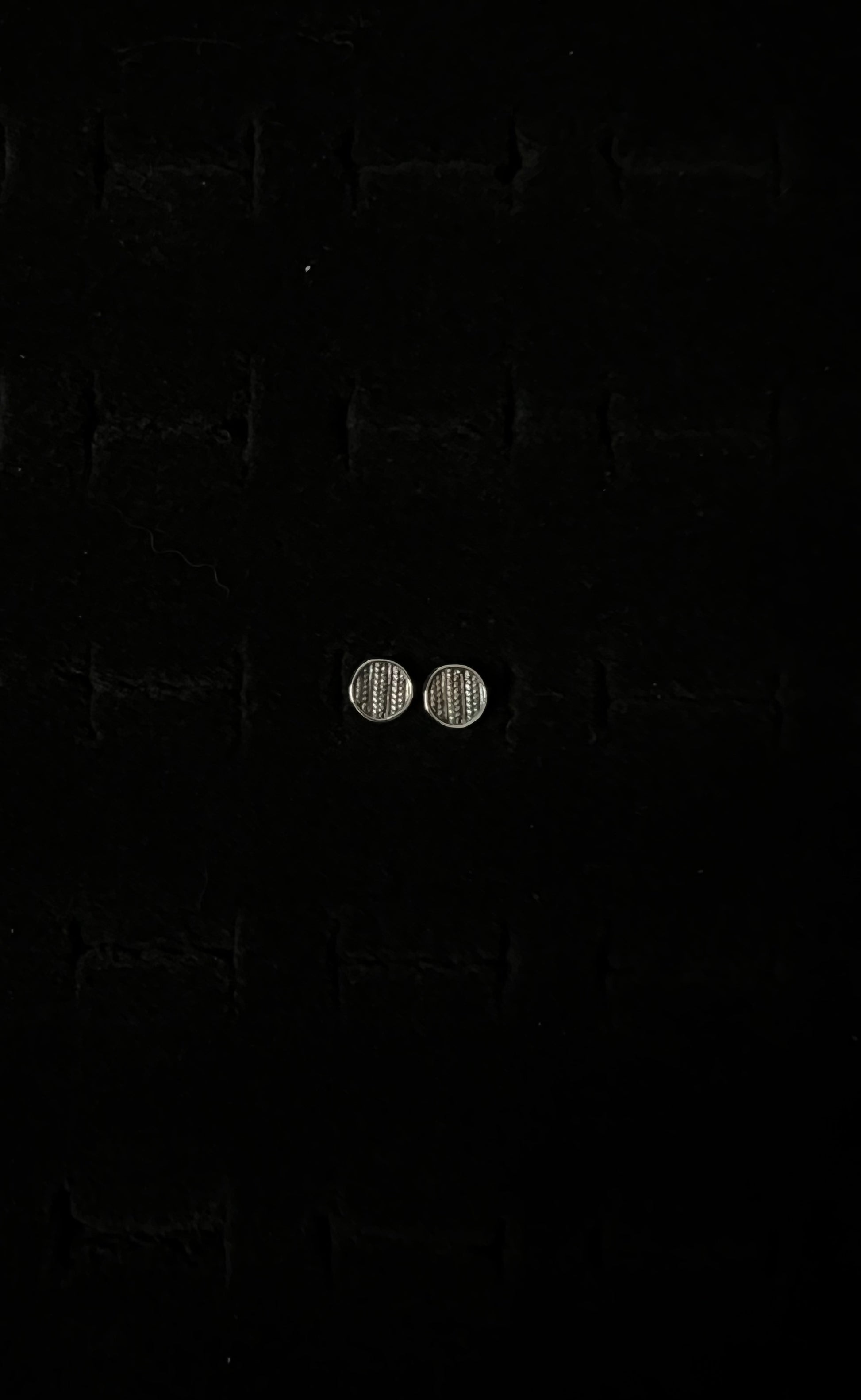 A close-up image of a pair of silver sweater post earrings on a textured black background.