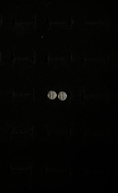 A close-up image of a pair of silver sweater post earrings on a textured black background.