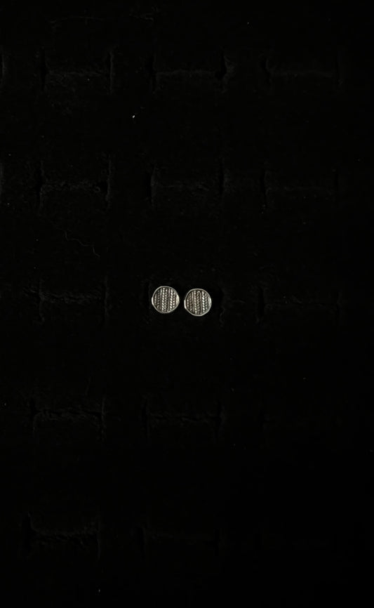 A close-up image of a pair of silver sweater post earrings on a textured black background.