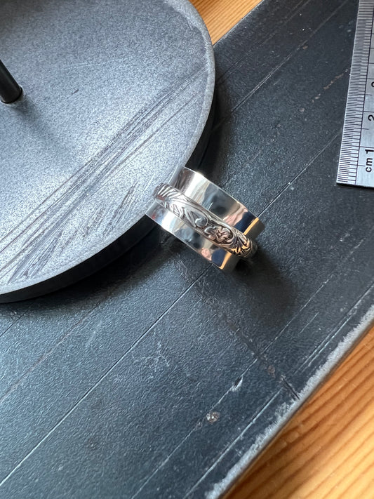 A sterling silver spinner ring with an intricately engraved design on the spinner, placed on a dark surface with a wooden edge.