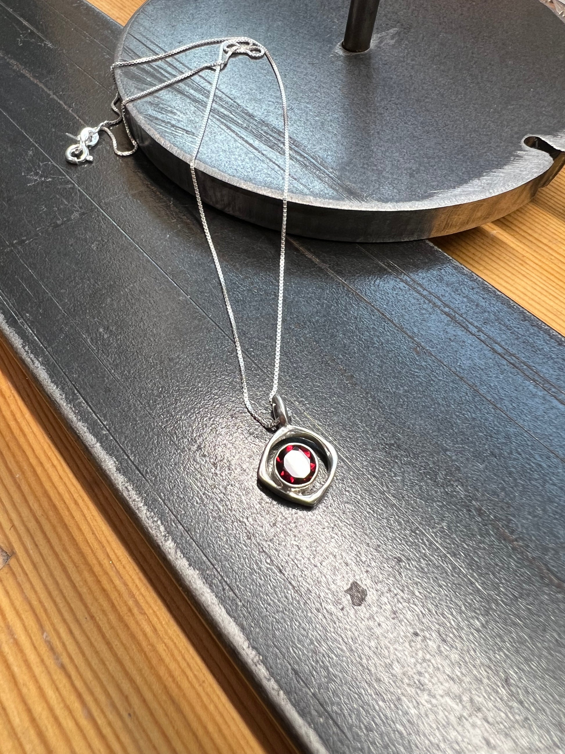 Square-Ring Pendant with Faceted Garnet – close-up of sterling silver square ring pendant showing faceted red garnet stone bezel detail, black background