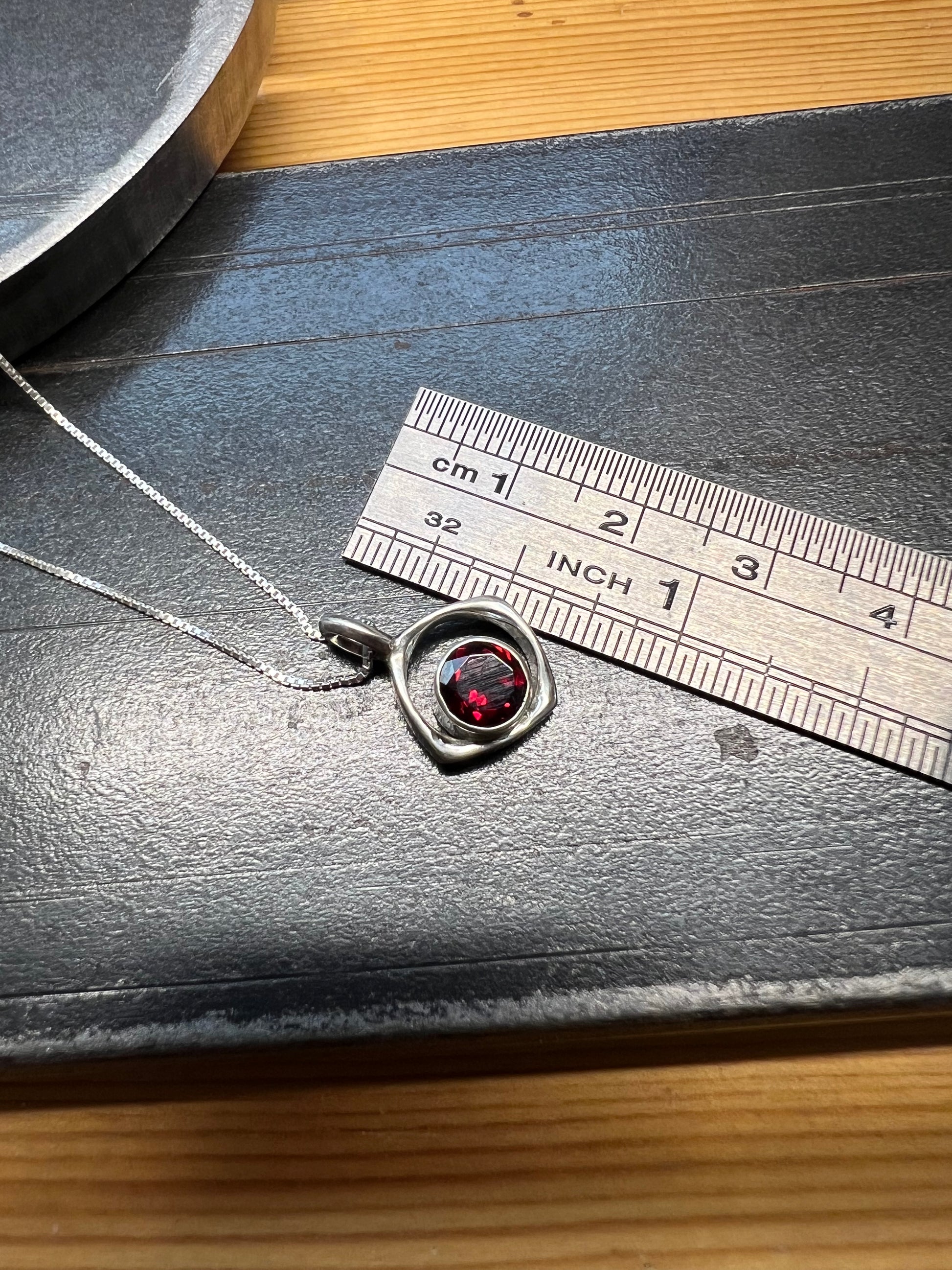 Square-Ring Pendant with Faceted Garnet – size reference showing sterling silver square-ring pendant with faceted garnet approximately 1 inch wide next to ruler, black background