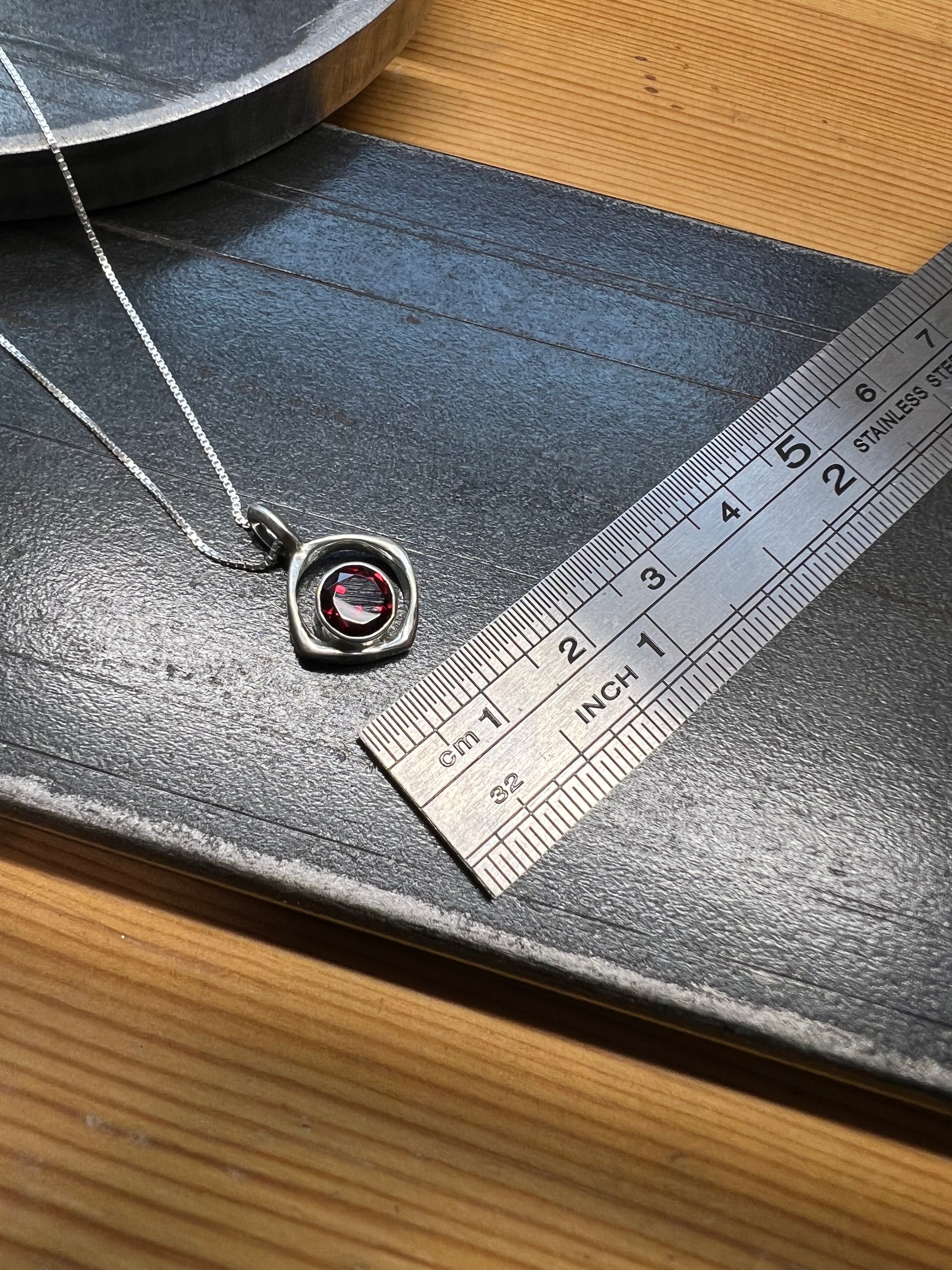 Square-Ring Pendant with Faceted Garnet – lifestyle shot of handcrafted sterling silver square-ring pendant with faceted red garnet worn on neck, black background