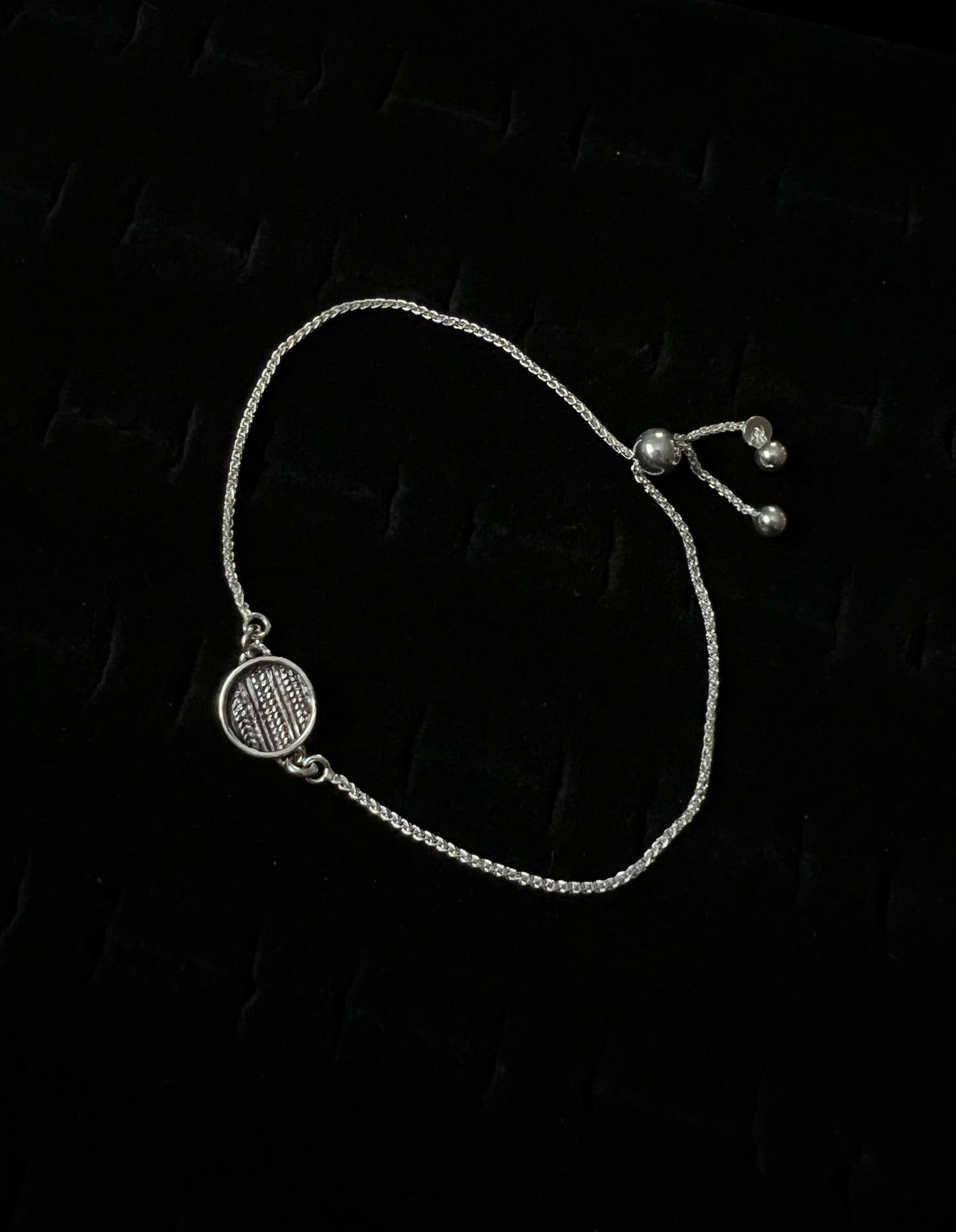 An adjustable sterling silver bracelet with a sweater pattern design on a dark background.