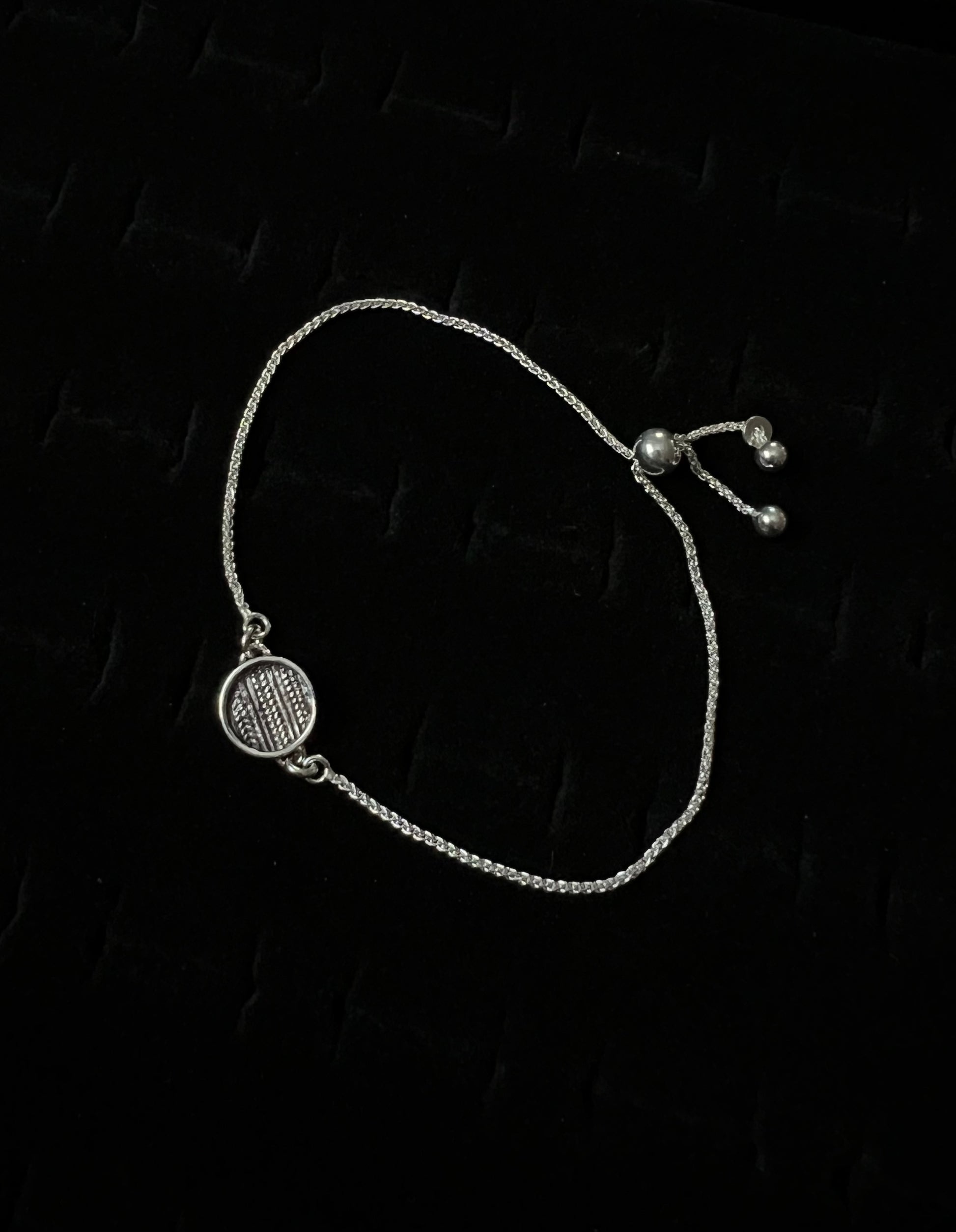 An adjustable sterling silver bracelet with a sweater pattern design on a dark background.