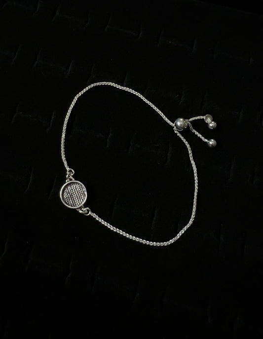 An adjustable sterling silver bracelet with a sweater pattern design on a dark background.