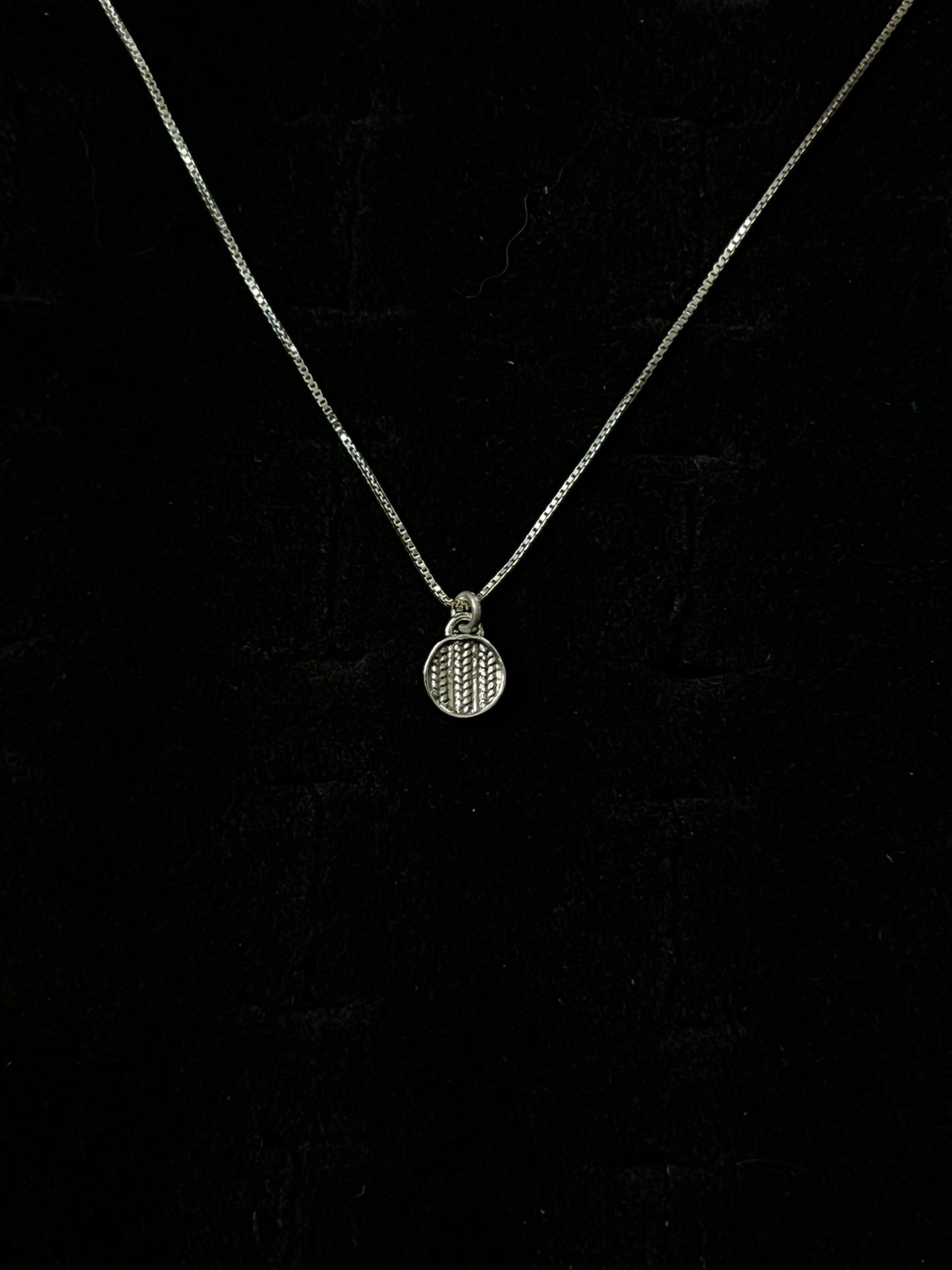 A silver necklace with a pendant designed to resemble a sweater, displayed against a black background.