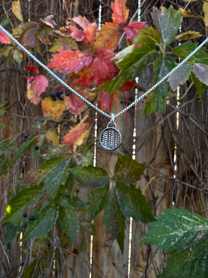 Sweater Charm Necklace – lifestyle shot of handcrafted sterling silver sweater-texture disc charm necklace worn on neck, black background