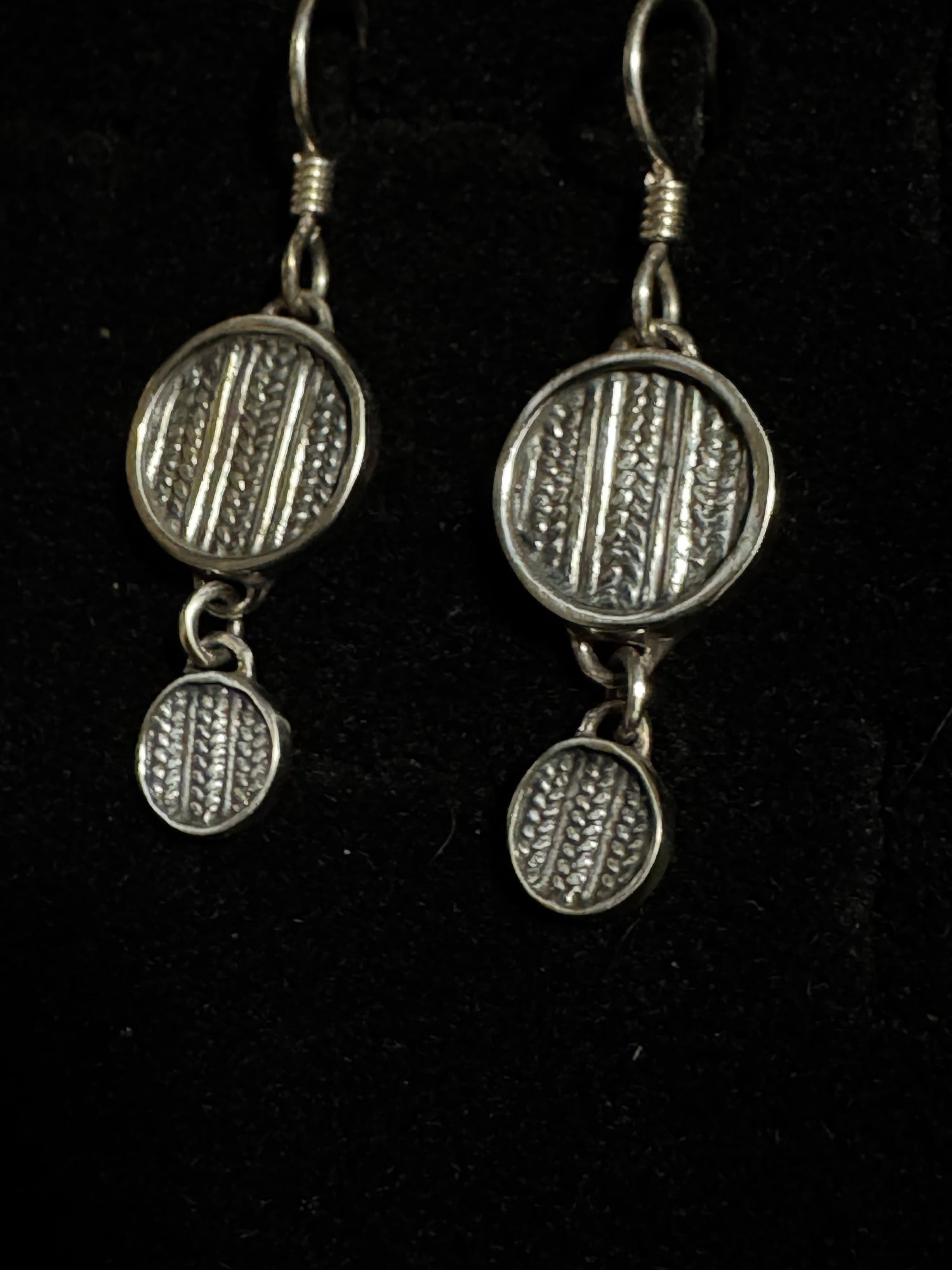 Pair of silver earrings with circular designs on a black background