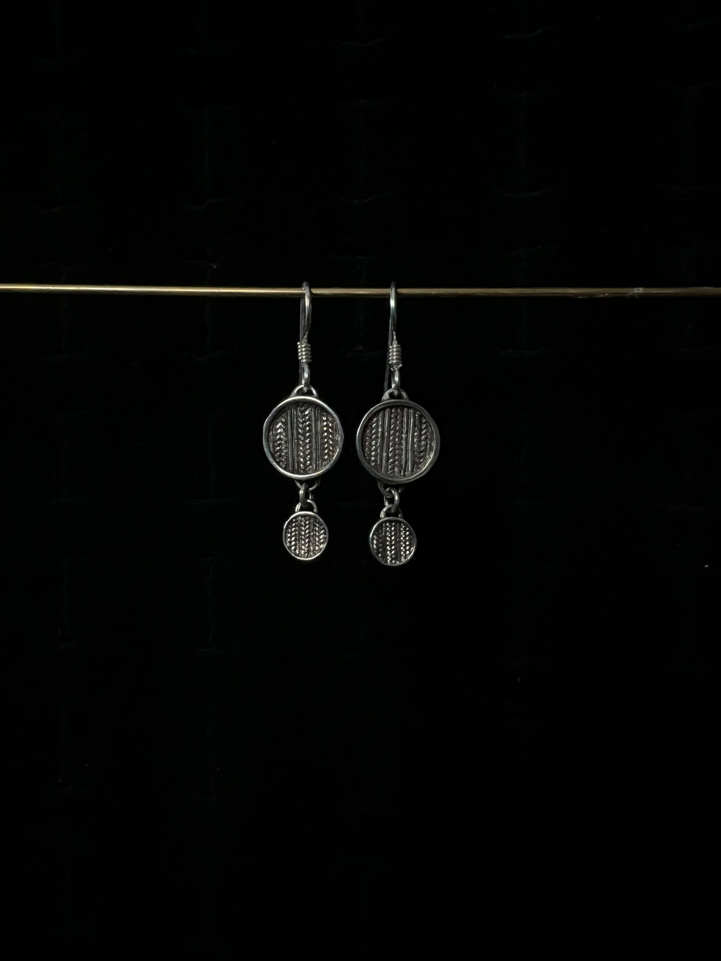 A pair of silver tiered sweater drop earrings displayed against a dark background.